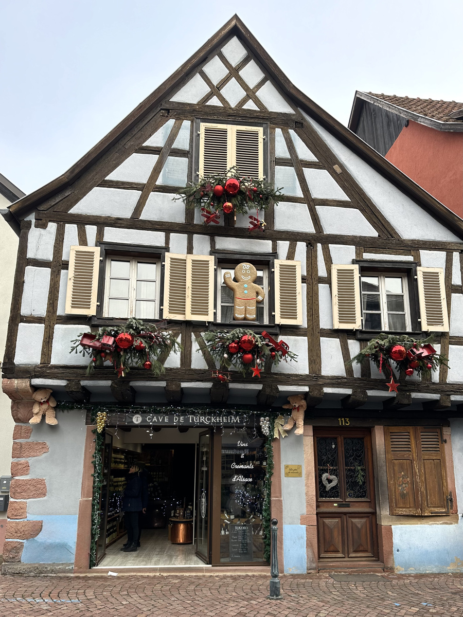 Half-timbered wine shop in Kaysersberg with a gingerbread figure, evergreen garlands and red Christmas ornaments.