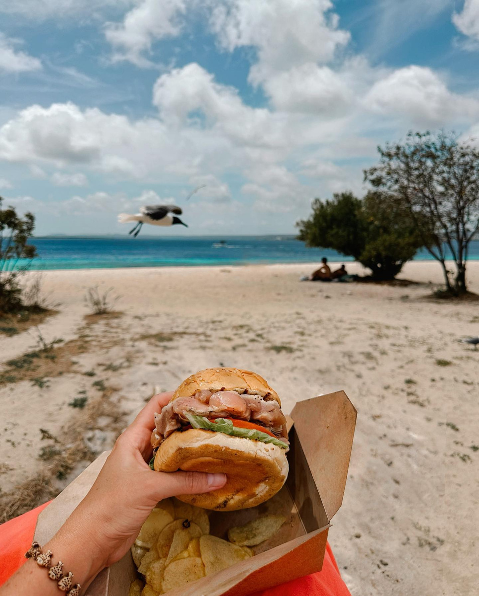 A tuna burger held above its paper tray beside the beach on Bonaire.