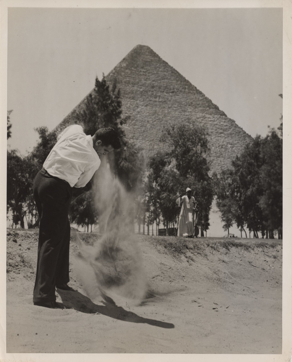 Eddie Niederhauser plays a bunker shot at Mena House in 1947, with a caddie and the Great Pyramid behind him.