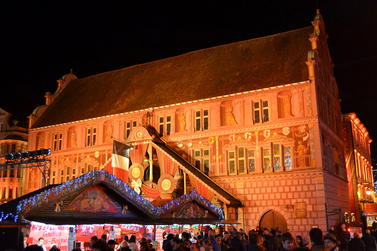 Mulhouse Town Hall illuminated at night, with patterned Christmas cloth draped over its staircase and market stalls below.