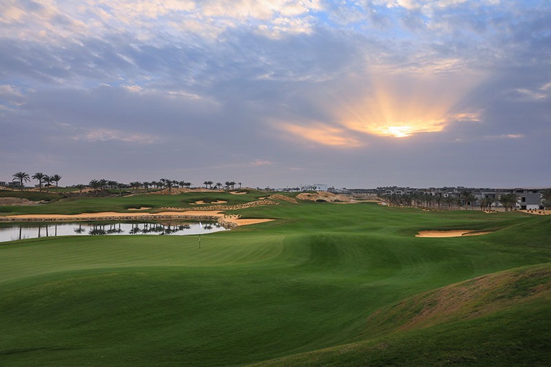 A lake beside NEWGIZA’s green fairways and sand bunkers, with houses along the horizon.
