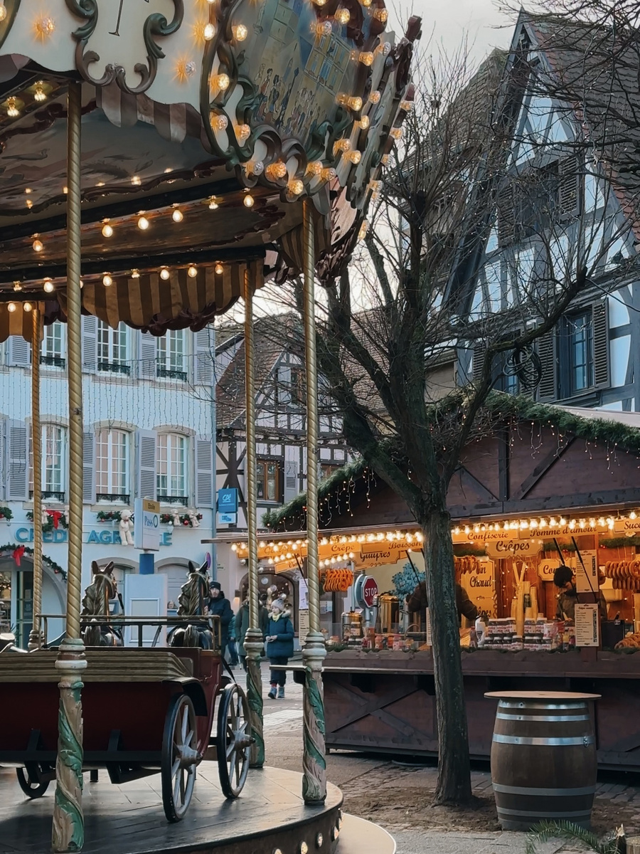 An illuminated carousel beside Christmas food stalls in Obernai’s historic centre.