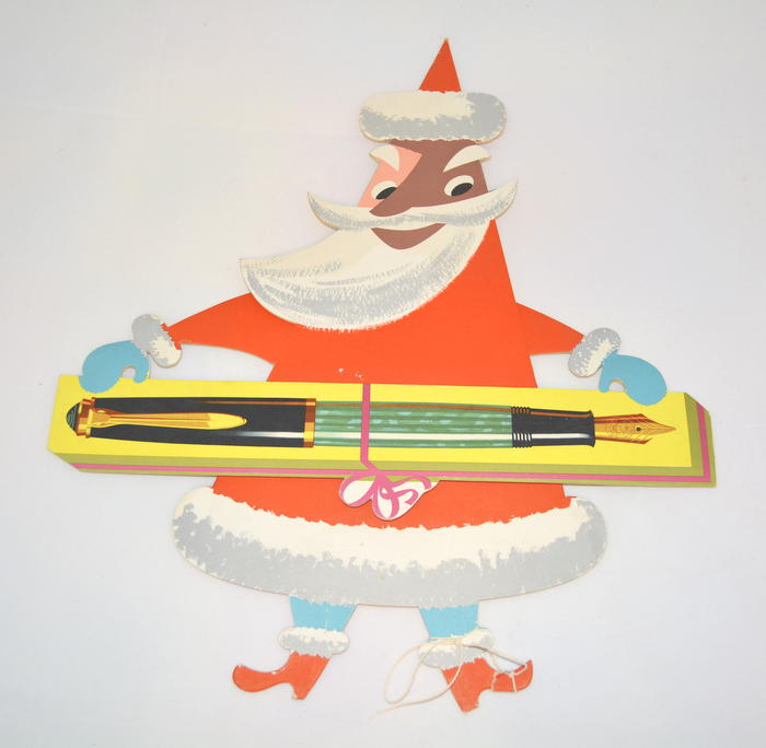 Cardboard Joulupukki advertising display in a red coat and blue gloves, holding a large green Pelikan fountain pen.