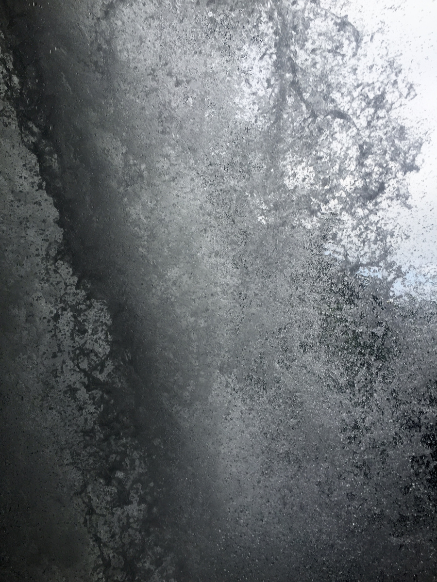 A close view of falling white water and dark rock from behind a waterfall