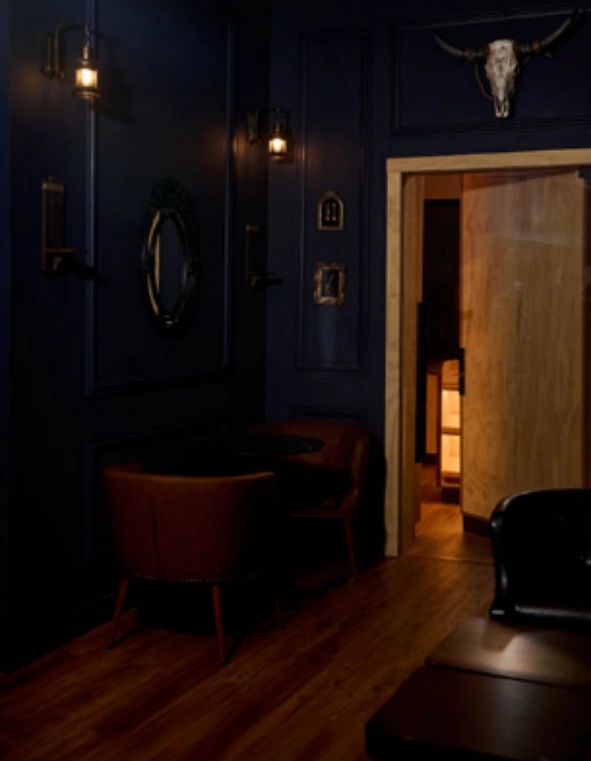 Leather armchairs and small tables in Prohibition’s dark-panelled lounge, beside an open wooden doorway.