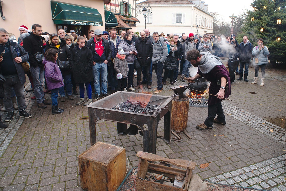 A blacksmith works glowing metal at an outdoor forge while visitors watch at Ribeauvillé’s medieval Christmas market.