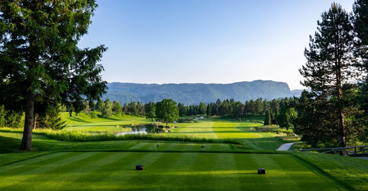 A tee on the King’s Course at Royal Bled looking down a fairway past a pond towards wooded hills.