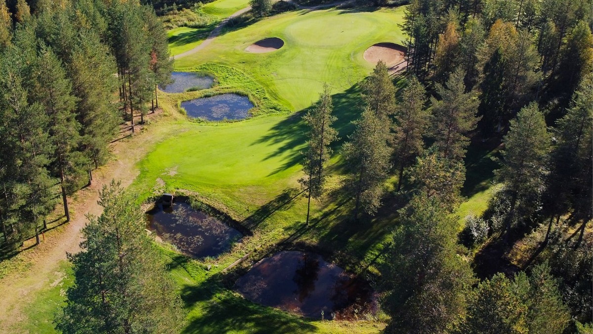 Aerial view of a green between two sand bunkers, with ponds and dense pine forest beside the fairway.