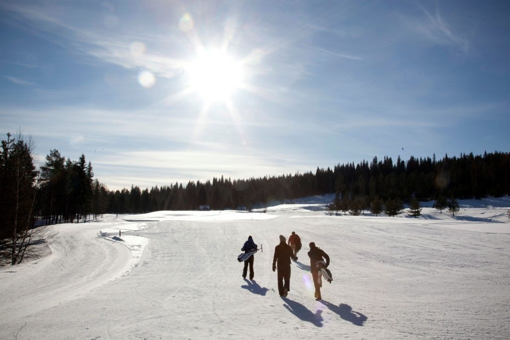 Four golfers carrying clubs across a groomed snow fairway in low winter sunshine.