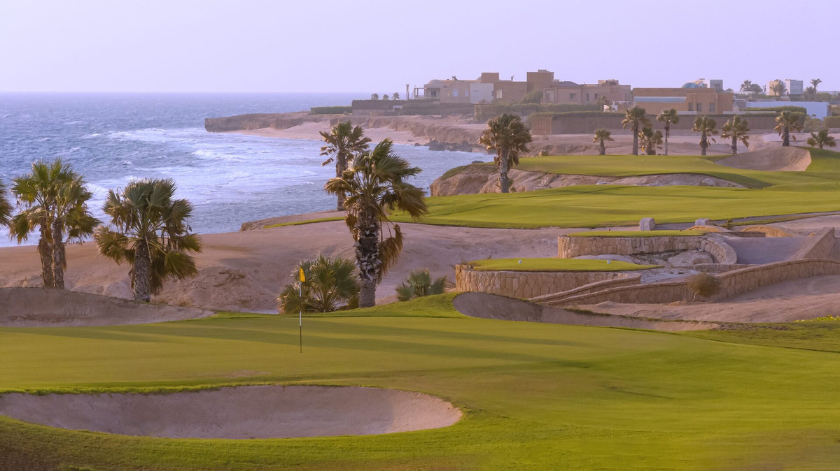 Greens and sandy gullies near Somabay’s fourteenth hole, with a stone bridge and the Red Sea beyond.