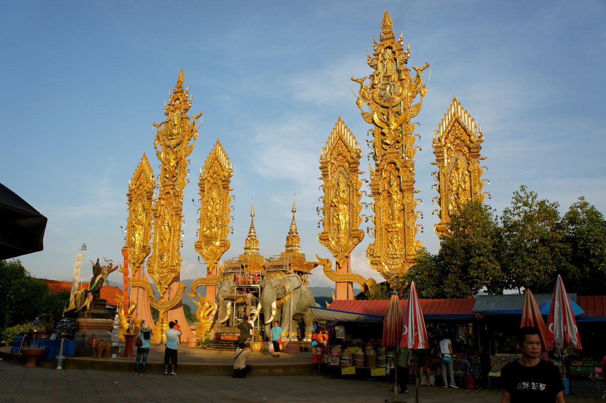 Tall gilded ornaments rise above elephant sculptures and visitors at the Golden Triangle riverside.