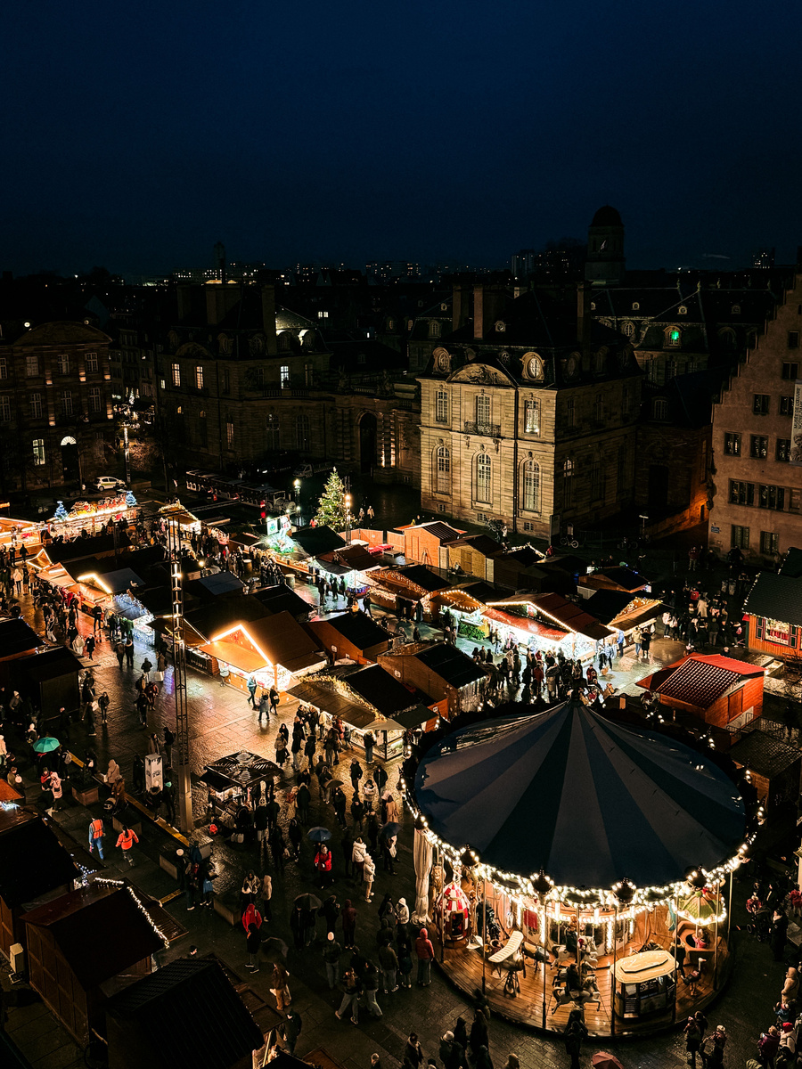 Illuminated Christmas stalls, visitors and a carousel in Strasbourg’s Place du Château, with Palais Rohan behind.
