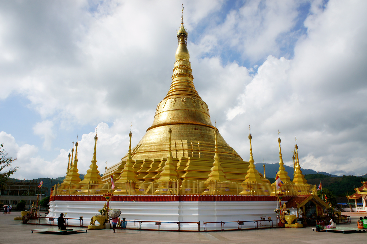 A golden pagoda and its surrounding terrace in Tachilek beneath a blue sky.