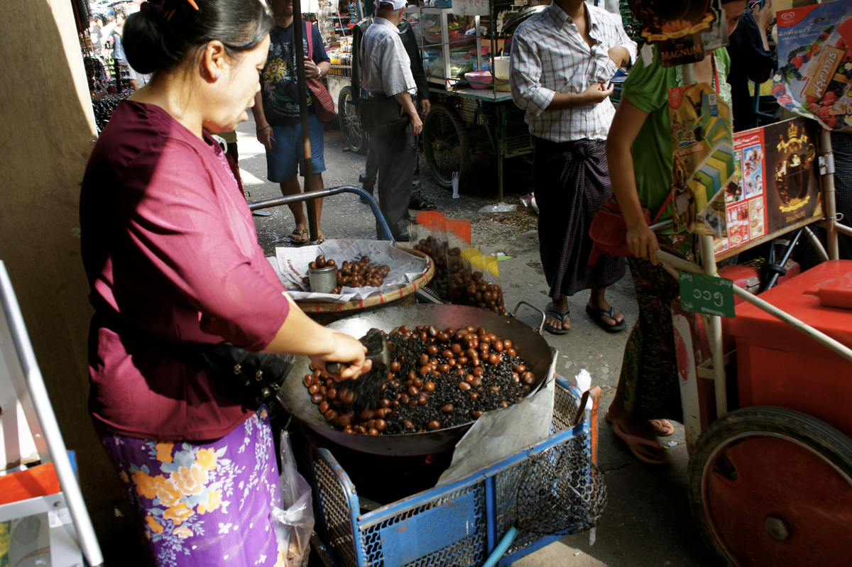A market vendor stirs chestnuts in a large pan as shoppers pass her stall in Tachilek.