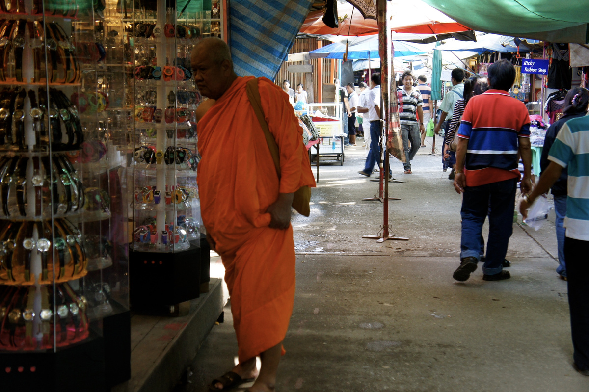 A monk in orange robes walks between covered market stalls in Tachilek.