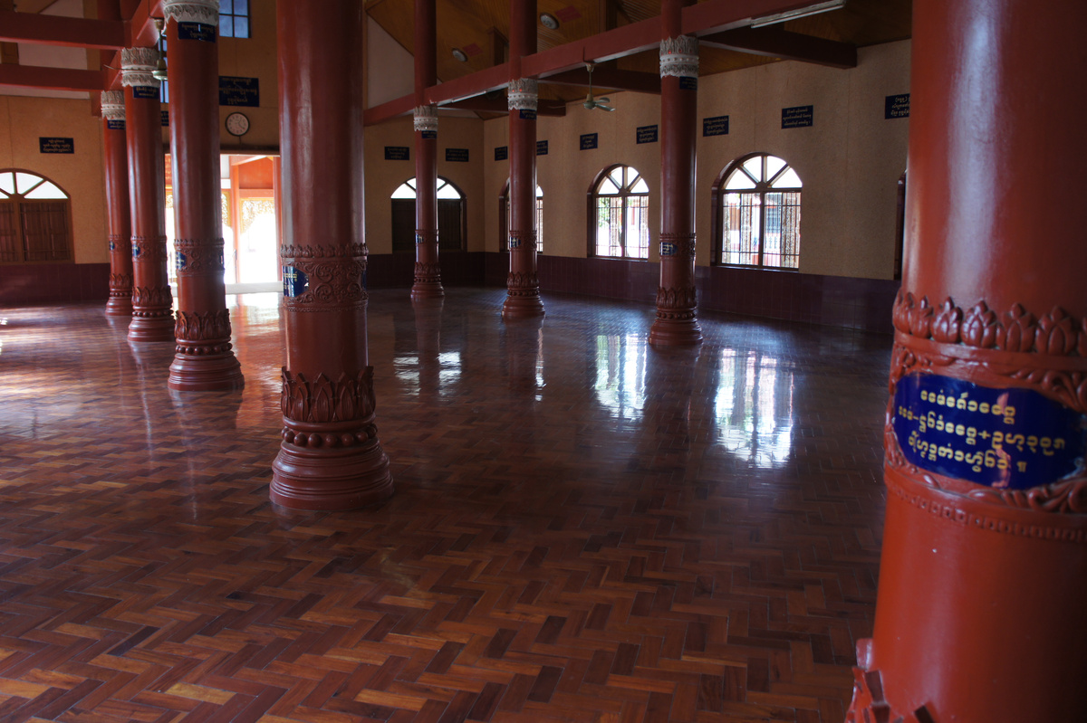 Red carved columns and arched windows surround the polished tiled floor of a temple hall in Tachilek.