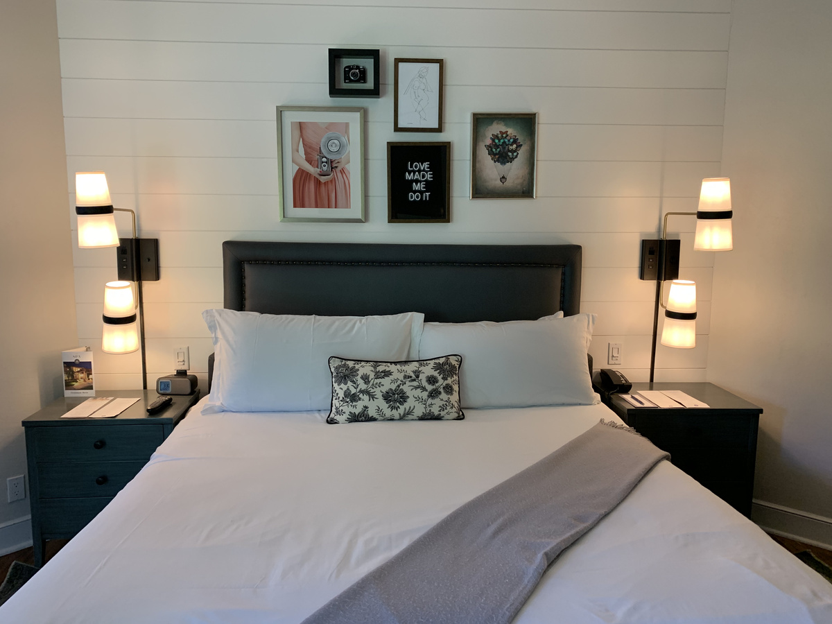 Our Vintage House bedroom with a dark headboard, wall lamps and framed pictures above the bed.