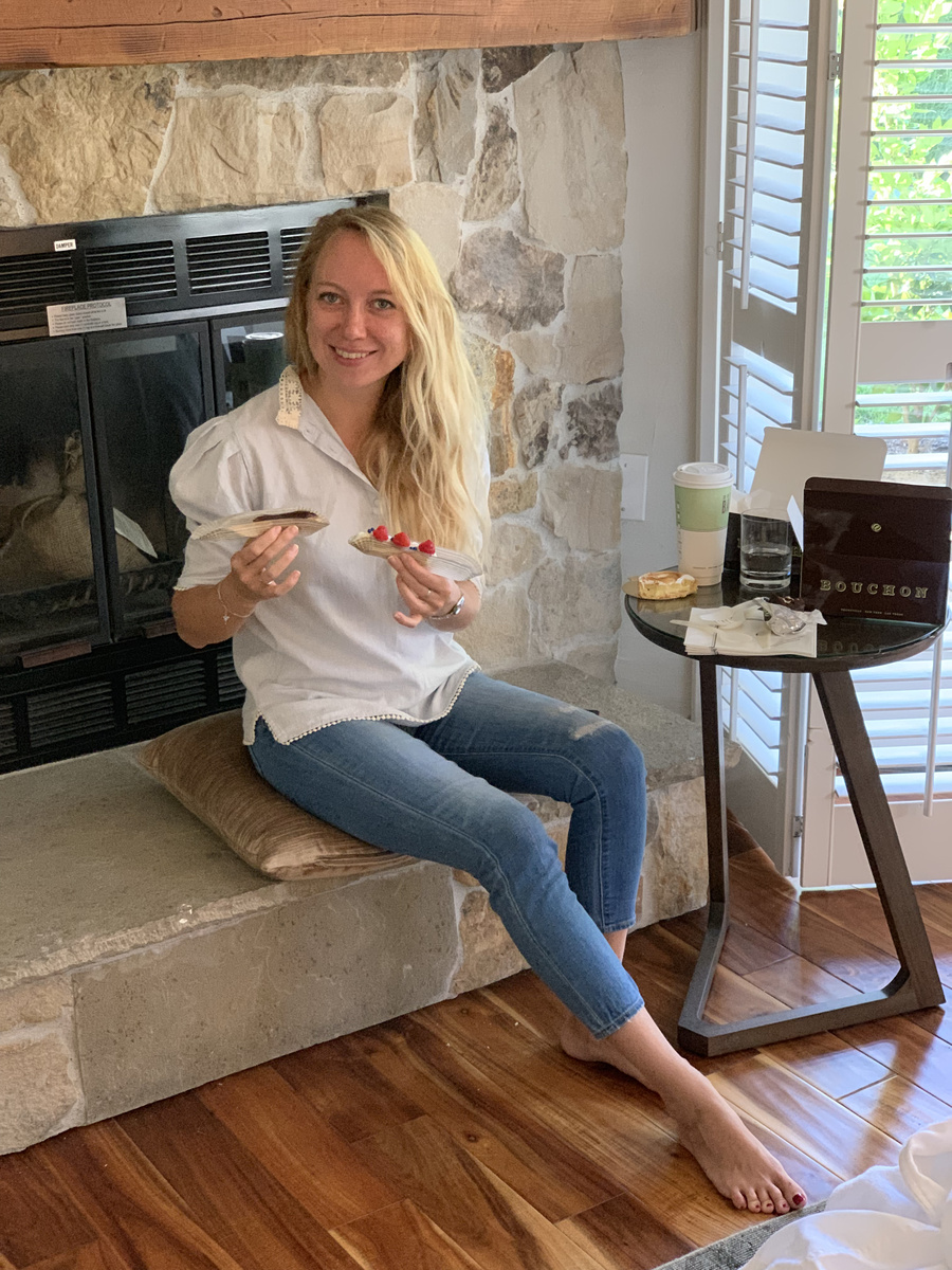Olga sitting on the stone hearth in her Vintage House room, holding raspberry pastry from Bouchon Bakery.