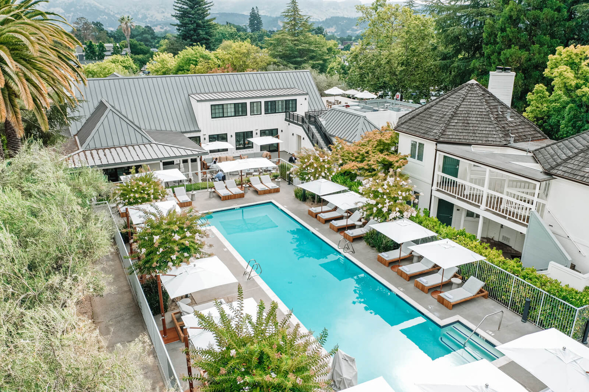Vintage House swimming pool surrounded by loungers, white parasols and garden buildings.