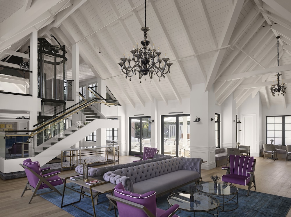 Vintage House’s double-height lounge with white roof beams, a black chandelier, purple armchairs and a staircase.