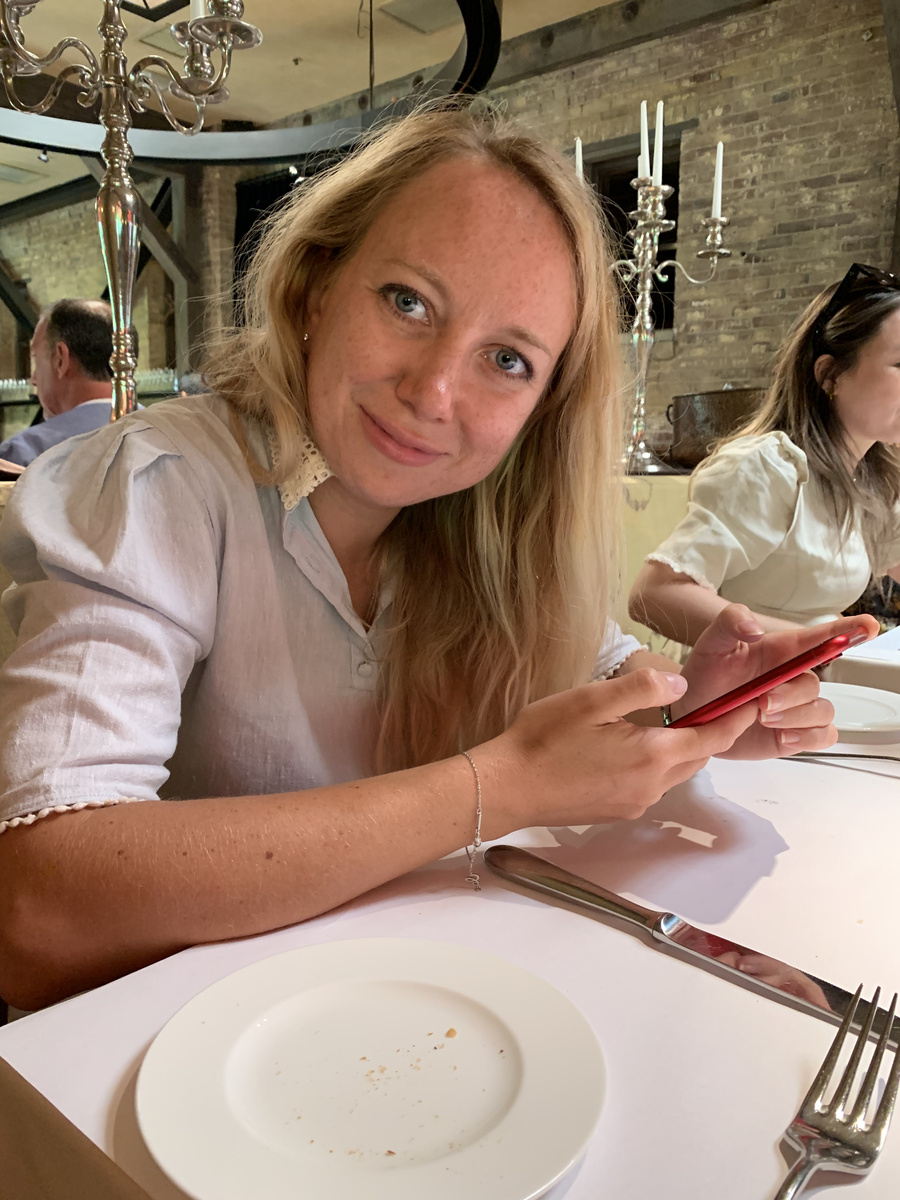 Olga at lunch in V Marketplace, Yountville, with a silver candelabrum and exposed brick behind her.
