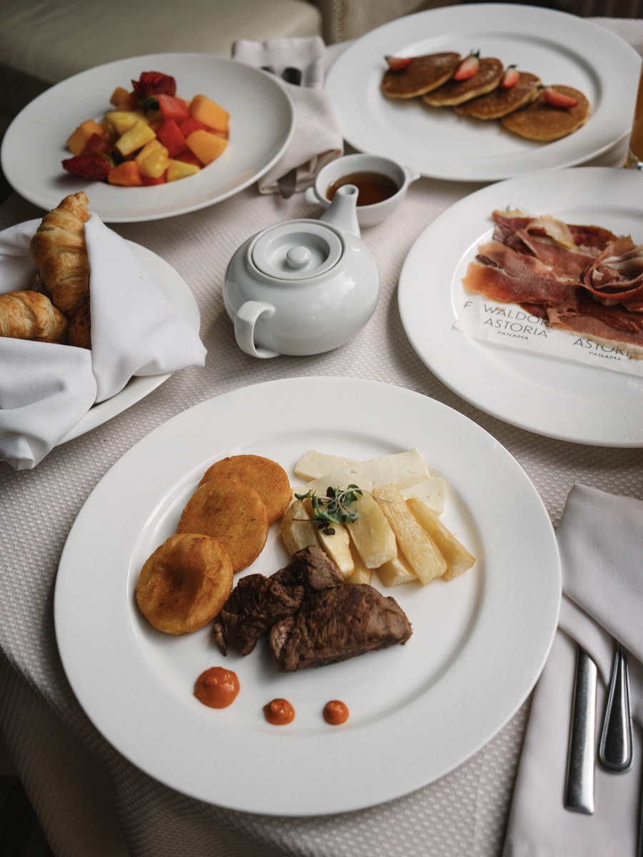 Room-service breakfast with fruit, pancakes, pastries and a hot dish on a white tablecloth.