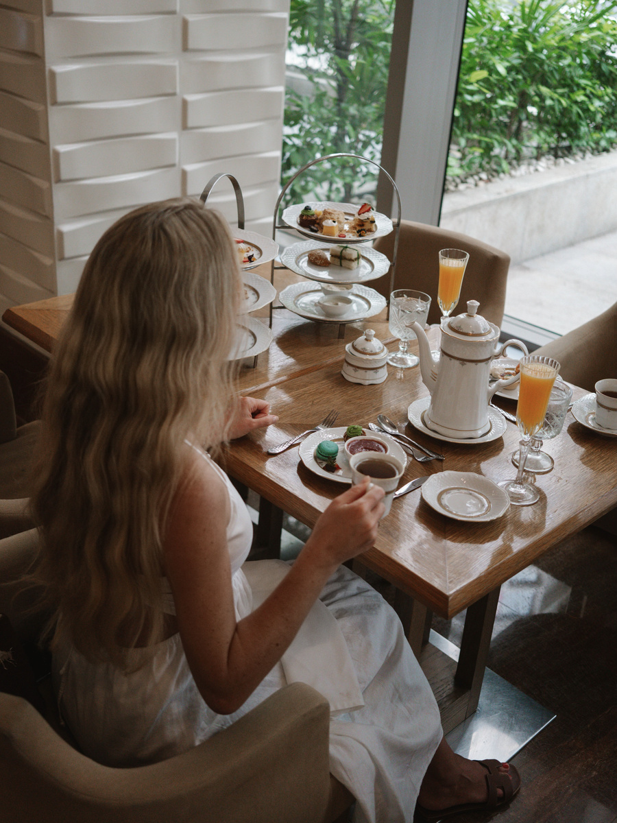 Olga seated at a table with afternoon-tea stands, china cups and a teapot at Peacock Alley.