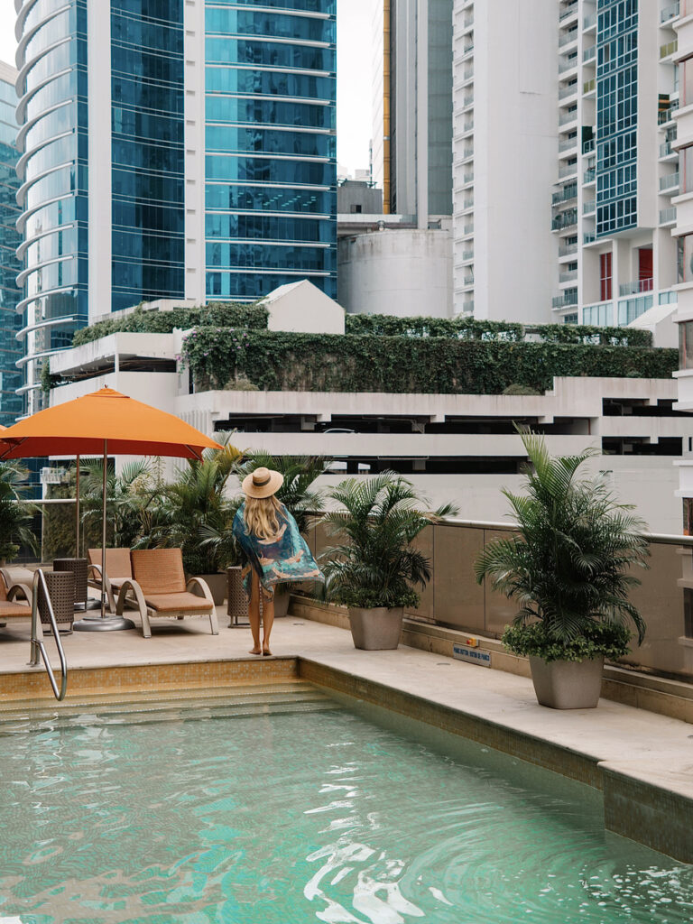 Olga beside the swimming pool, with potted palms and Panama City towers behind her.
