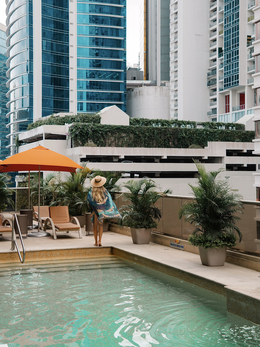 Olga beside the swimming pool, with potted palms and Panama City towers behind her.